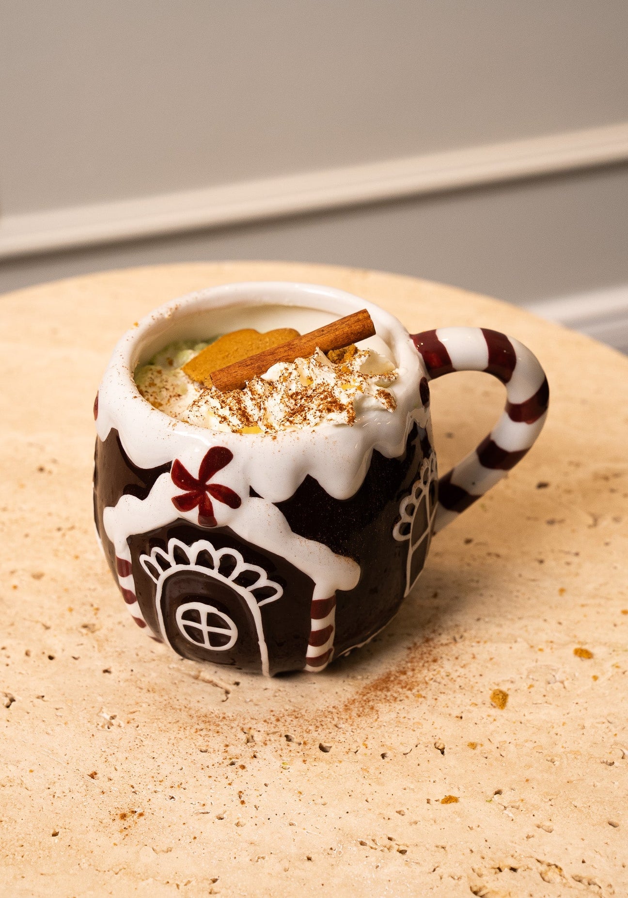 Festive mug of matcha latte with whipped cream, cinnamon stick, and cookie on a table