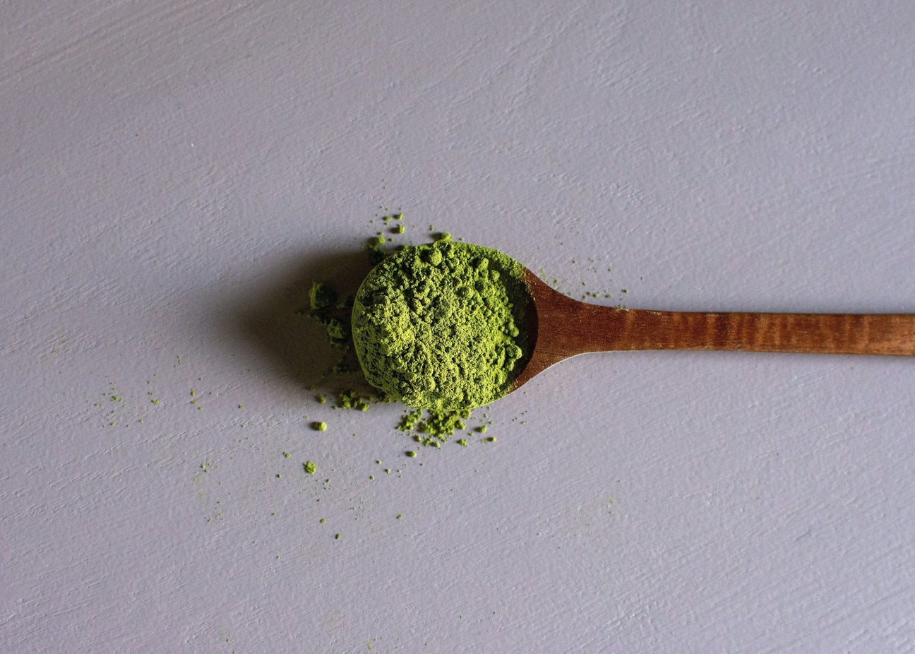 Wooden spoon with bright green matcha powder on a light surface