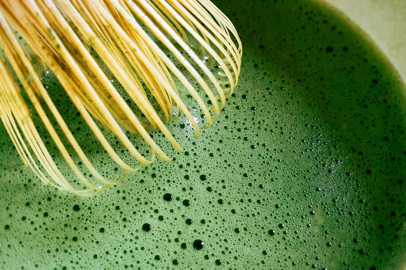 Close-up of bamboo whisk mixing frothy ceremonial grade matcha tea
