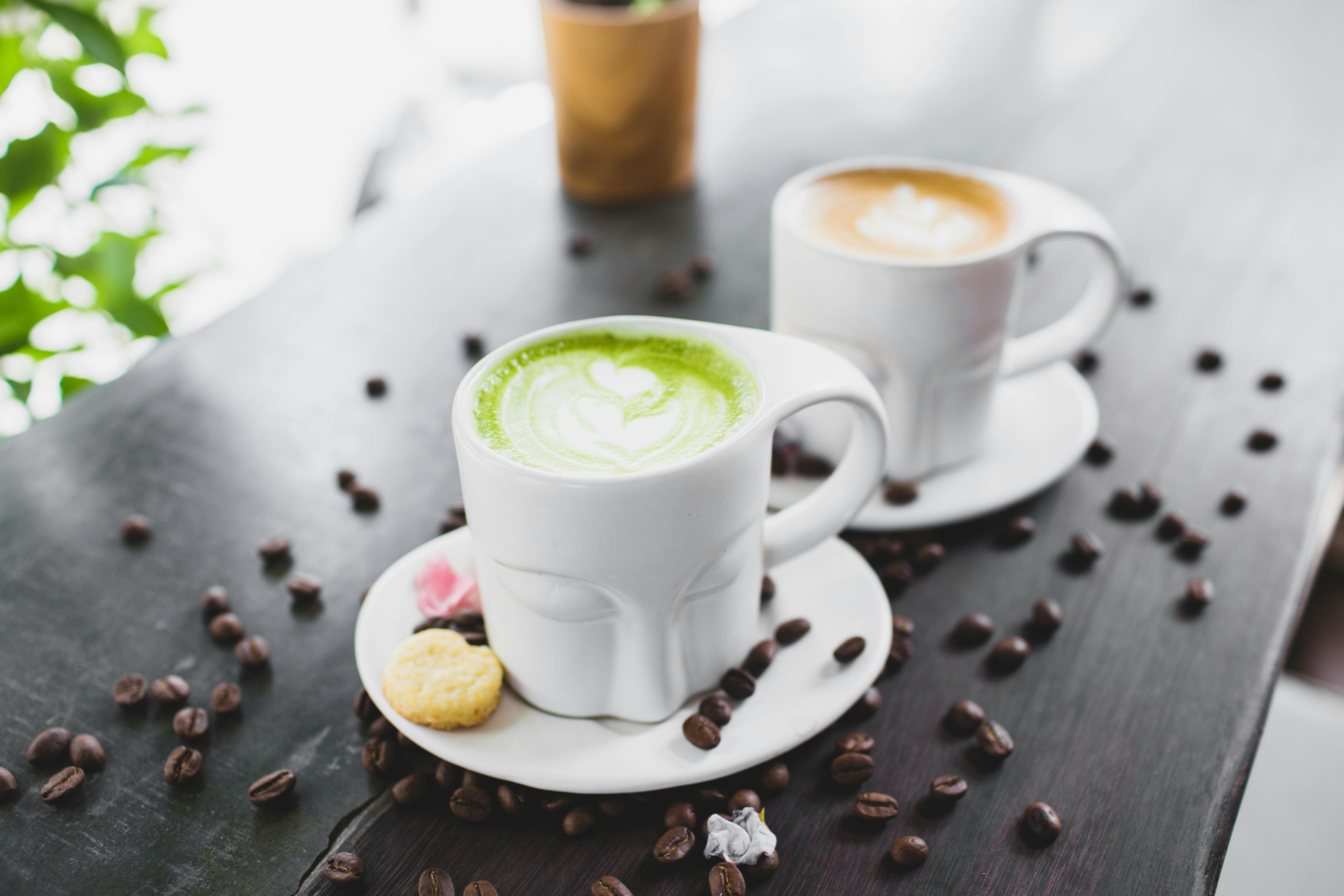 Ceremonial grade matcha latte with heart latte art in white cup on wooden table with coffee beans