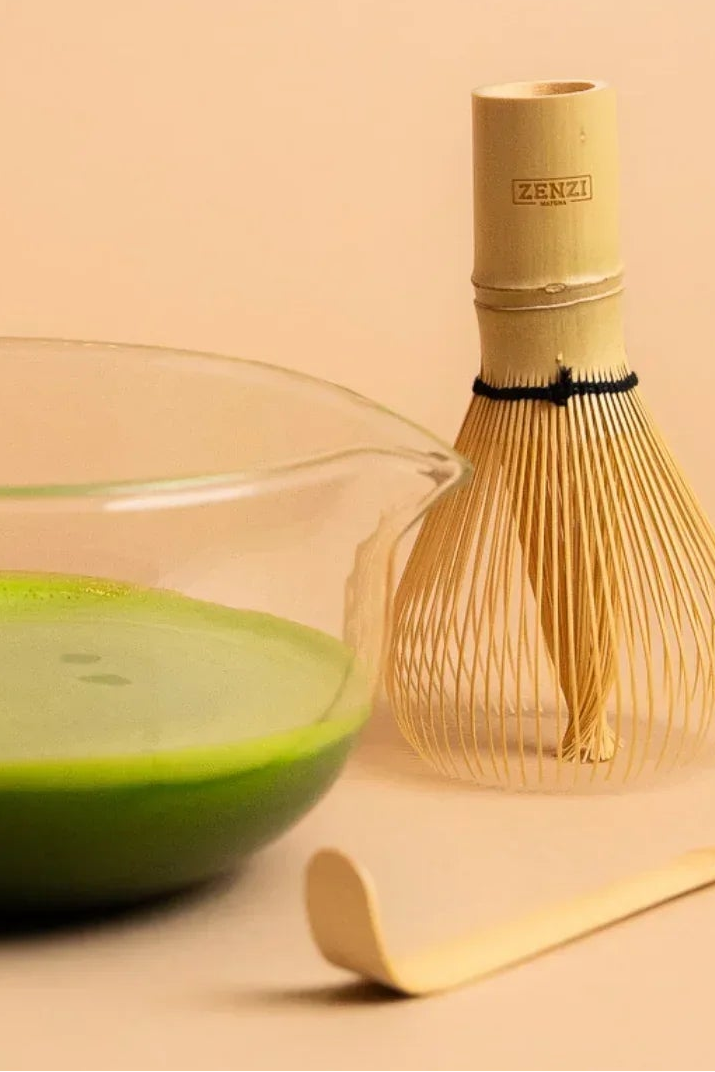 Ceremonial matcha tea in glass bowl with bamboo whisk and scoop on beige background