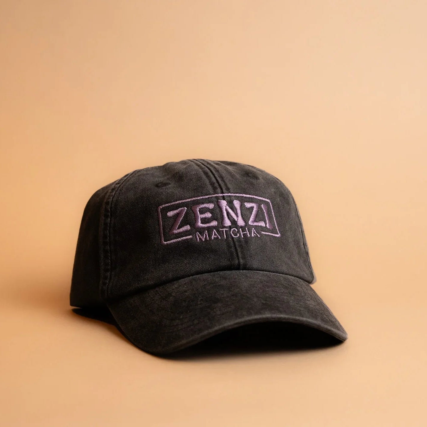 Black baseball cap with Zenzi Matcha embroidered logo on beige background