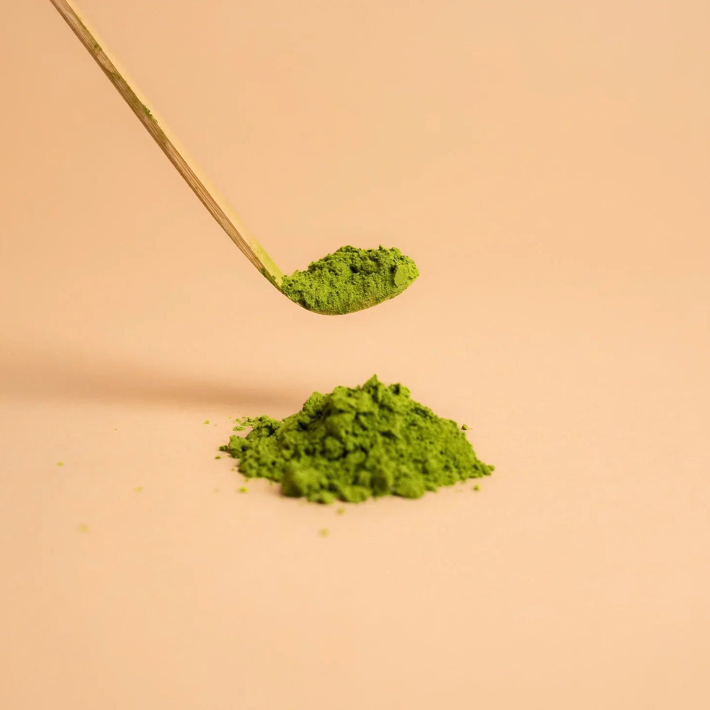 Ceremonial grade matcha green tea powder with bamboo spoon on beige background